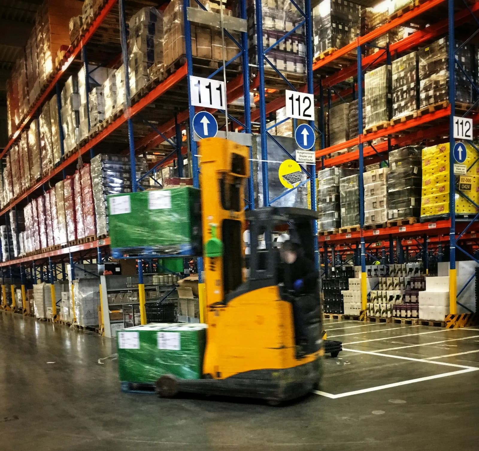 Reach forklift moving through a warehouse aisle lined with pallet racking