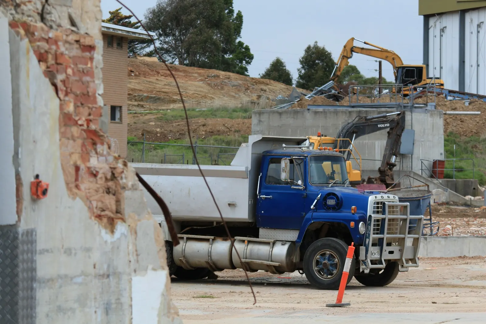 Blue tipper truck parked on a construction site with an excavator behind it